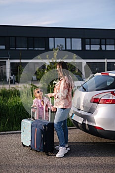 Mom and daughter stand near the car with their suitcases and waiting for the trip. Family journey