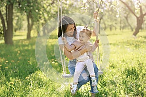 Mom and daughter swinging  on a swing in a blooming garden on a hot spring day. The child has fun with his mother.