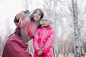 Mom and daughter take a selfie in the park. The child walks with his mother in winter. People in pink clothes take pictures of