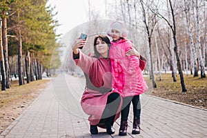 Mom and daughter take a selfie in the park. The child walks with his mother in winter. People in pink clothes take pictures of