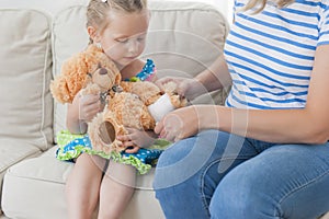 Mom and daughter together on the couch playing with teddy bear.