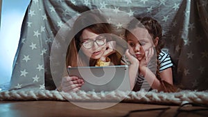 Mom and daughter under the blanket with a digital tablet. kid dream online video games at concept. Mom and daughter