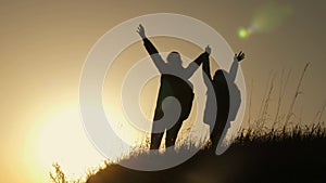 Mom and daughter on vacation traveling and dancing on mountain. Woman with raised hands on top of mountain looking at