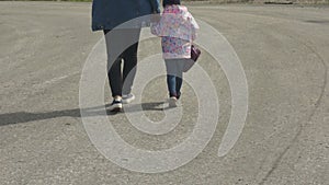 Mom and daughter are walking along the road holding hands together