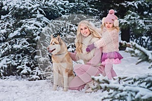 Mom and daughter walking a dog of the Husky breed in a snowy park