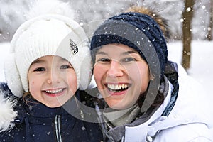 Mom and daughter in warm clothes in the snowy forest hugging and looking into the frame. Winter entertainment outside, active