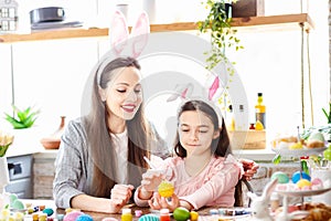 Mom and daughter wearing bunny ears decorating Easter eggs.