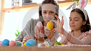 Mom and daughter wearing bunny ears decorating Easter eggs.