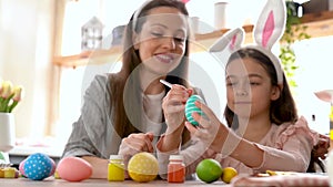 Mom and daughter wearing bunny ears decorating Easter eggs.