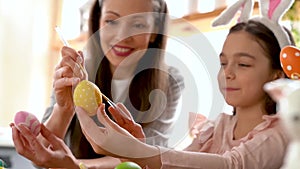 Mom and daughter wearing bunny ears decorating Easter eggs.