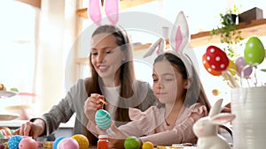 Mom and daughter wearing bunny ears decorating Easter eggs.