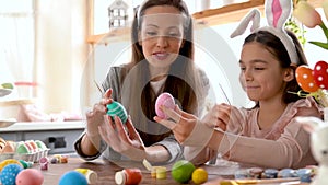 Mom and daughter wearing bunny ears decorating Easter eggs.