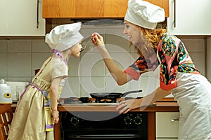 Mom and daughter in white chef hats cook in the kitchen.
