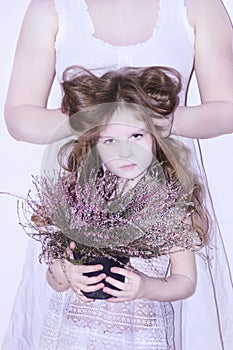 Mom and daughter in white dresses on a white background depict winter and spring, holding flowers and a twig with leaves.