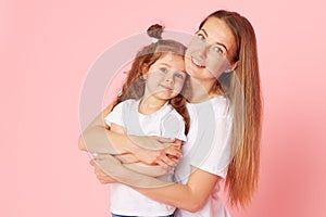 Mom and daughter in white t-shirts and jeans play and hug on a pink background. Caring for loved ones. photo