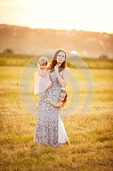 Mom with daughters stand and hug on mowed field