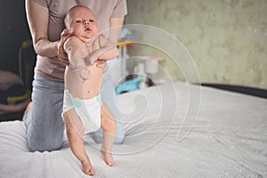 Mom doing exercises for baby in diaper. Cute emotional funny newborn boy learns to walk