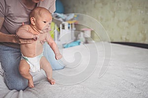 Mom doing exercises for baby in diaper. Cute emotional funny newborn boy learns to walk