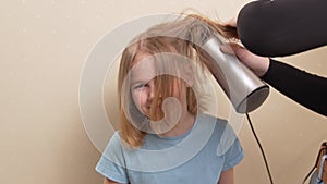 mom dries her daughter's hair with a hair dryer with a comb attachment.