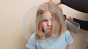 mom dries her daughter's hair with a hair dryer with a comb attachment.