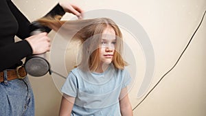 mom dries her daughter's hair with a hair dryer with a comb attachment.