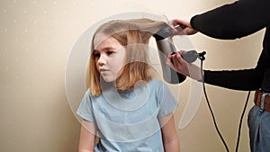 mom dries her daughter's hair with a hair dryer with a comb attachment.