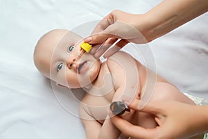 Mom drops her nose to a newborn baby. sick child, baby staying in bed, mom giving him medicine and checking for fever. sick infant