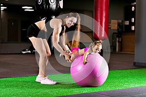Mom is engaged with her daughter in the gym with a fitness ball.