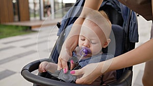 Mom fastens the baby in the stroller for safety on a summer day. A little boy is strapped into a wheelchair. Attachments