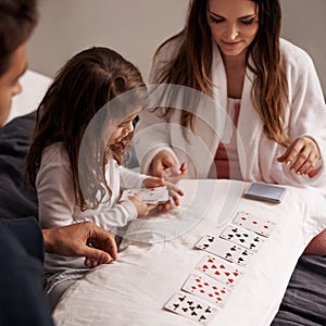 Mom, father and girl with playing cards for game with bonding, learning and relax with strategy in bedroom. Dad, mother