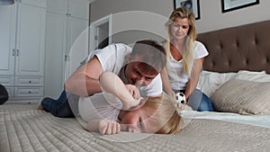 Mom and father tickling her child. people, family, fun and morning concept - happy child with parents tickling in bed at