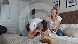 Mom and father tickling her child. people, family, fun and morning concept - happy child with parents tickling in bed at