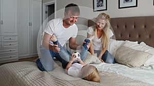 Mom and father tickling her child. people, family, fun and morning concept - happy child with parents tickling in bed at