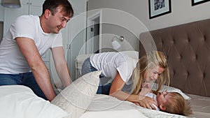 Mom and father tickling her child. people, family, fun and morning concept - happy child with parents tickling in bed at