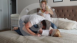 Mom and father tickling her child. people, family, fun and morning concept - happy child with parents tickling in bed at