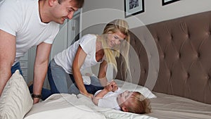 Mom and father tickling her child. people, family, fun and morning concept - happy child with parents tickling in bed at