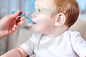 Mom feeding the baby holding hand with a spoon of food in the kitchen. Healthy baby nutrition. Emotions of a child