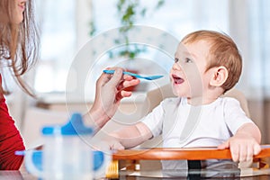 Mom feeding baby holding hand with a spoon of porridge. Emotions of a child while eating healthy food