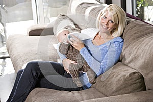 Mom feeding bottle to baby at home on couch