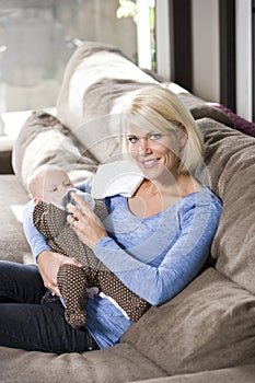 Mom feeding bottle to baby at home on couch