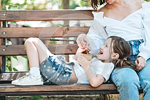 Mom feeds her little daughter ice cream in the park