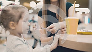 Mom feeds a little daughter with a fork, they sit in a cafe