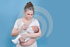 Mom feeds a newborn baby with a bottle feeding mixture on a blue background. Mother with a child boy in her arms, studio shot
