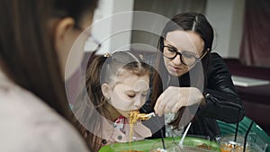 Mom feeds younger daughter with a fork in a cafe. Family lunch in the cafe.