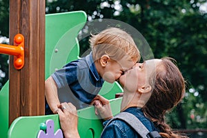 Mom gently kisses her baby in the pubic. They relax on the playground.