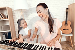 Mom and girl are playing the synthesizer at home. They rest and have fun.