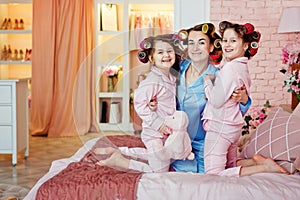 Mom and the girls are sitting on the bed in pink curlers and blue pajamas. Pajama party