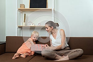 Mom gives her little daughter gift box. Mom and baby look into an open box. Holiday