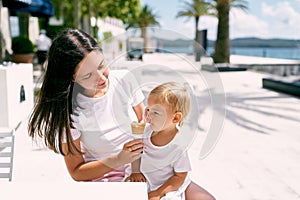 Mom gives the little girl ice cream while sitting at the table by the sea