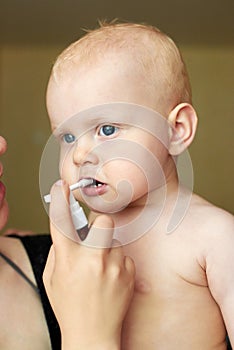 Mom gives medicine to a child with oral spray, treatment of sore throat and other diseases